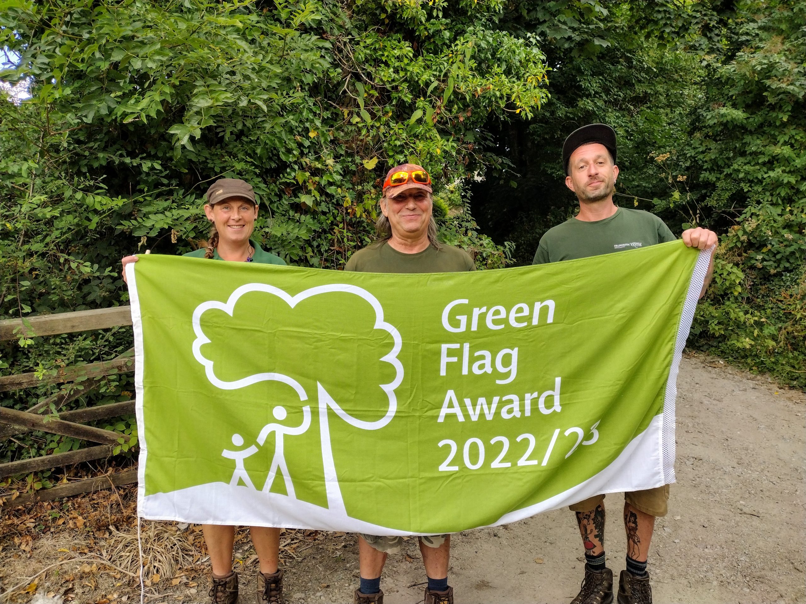Three members of the Grounds team hold the Green Flag