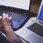 Man working on two laptops at once with his hands on a keyboard