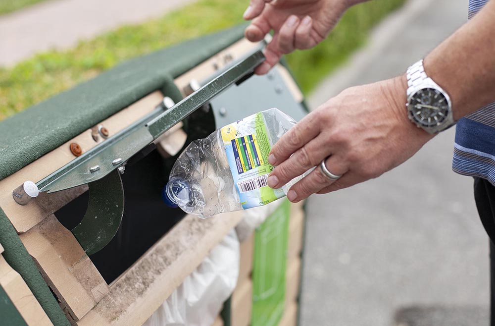 Image of a hand with a squashed plastic bottle putting it into a recycling bin