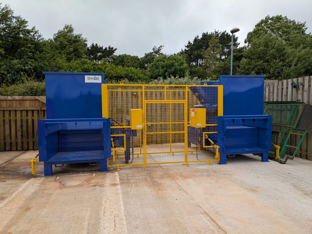 Two new, blue metal waste compactors joined by a yellow caging area in the waste compound on Penryn campus.